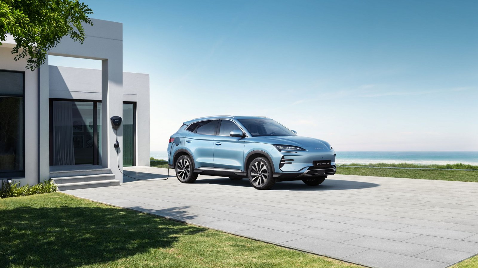 BYD SEAL U Elektro-SUV in hellblau parkt vor modernem Haus mit Blick auf Meer