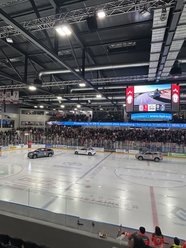 Eishockeyarena mit Zuschauern, drei Autos auf dem Eis und einer großen Anzeigetafel mit Werbung für BYD