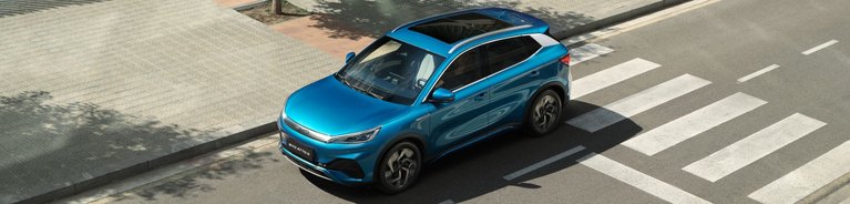 Der BYD ATTO 3 in der Farbe „Surfing Blue“ fährt in einer städtischen Umgebung auf der Straße. Sicht ist seitlich erhöht von oben.