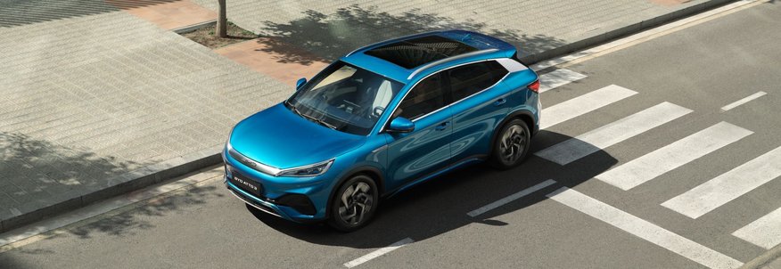 Der BYD ATTO 3 in der Farbe „Surfing Blue“ fährt in einer städtischen Umgebung auf der Straße. Sicht ist seitlich erhöht von oben.